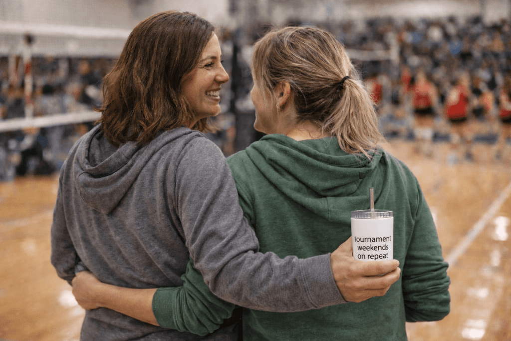 This is a shot of two moms hugging on the sidelines while watching their kids play volleyball.